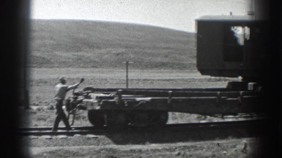 Worker in period attire stands beside the railcar, appearing to signal during the 1936 California rail construction footage.
