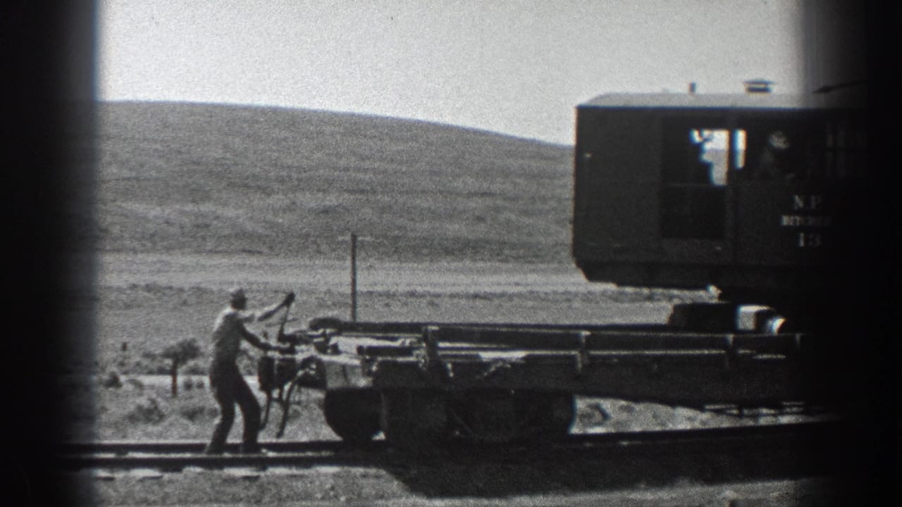 1936 California 8mm frame showing a man working a handcar or flatcar on rural railway track with a marked rail vehicle nearby.