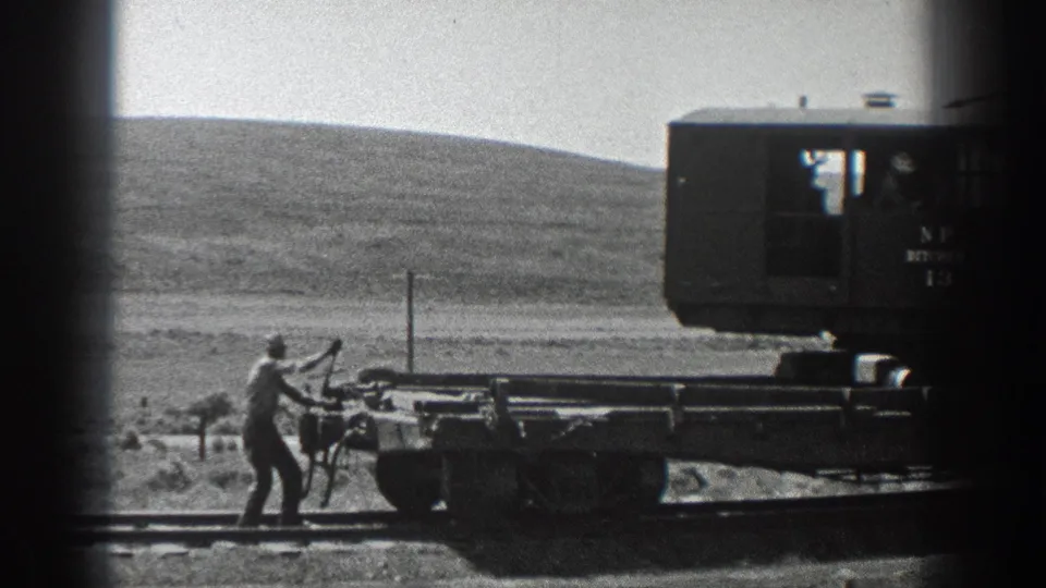 1936 California 8mm frame showing a man working a handcar or flatcar on rural railway track with a marked rail vehicle nearby.