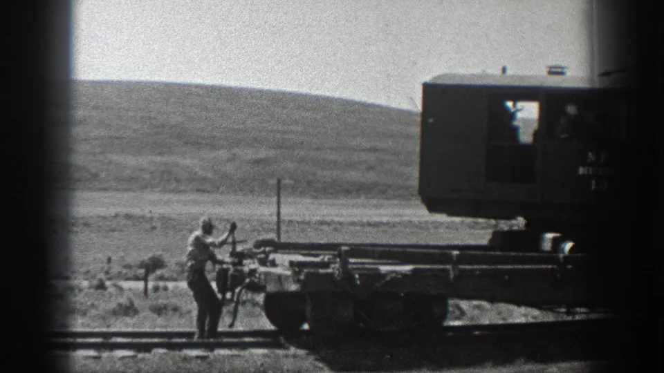 Black-and-white 1936 California home-movie frame of a worker handling rail equipment on open rural track.