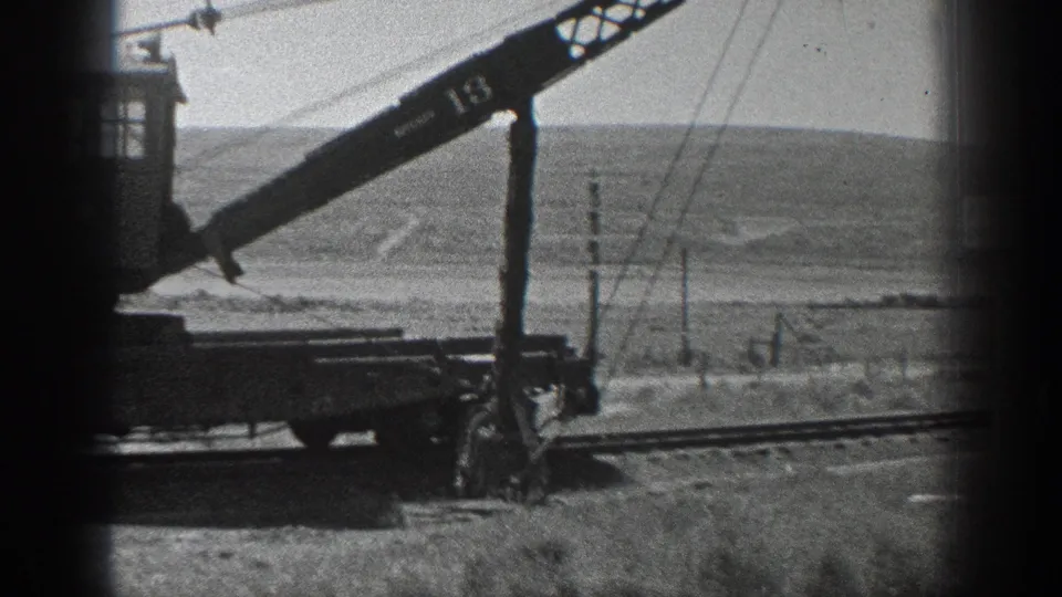 Black-and-white 1936 California frame showing a rail crane on rural track, with poles and rolling hills behind it.