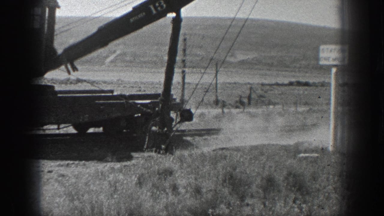 1936 California 8mm frame showing a numbered railcar crane working near tracks, utility poles, open hills, and a STATION ONE MILE sign.