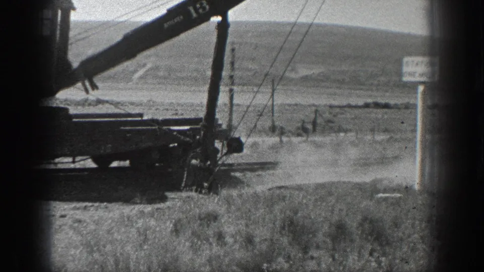 1936 California 8mm frame showing a numbered railcar crane working near tracks, utility poles, open hills, and a STATION ONE MILE sign.