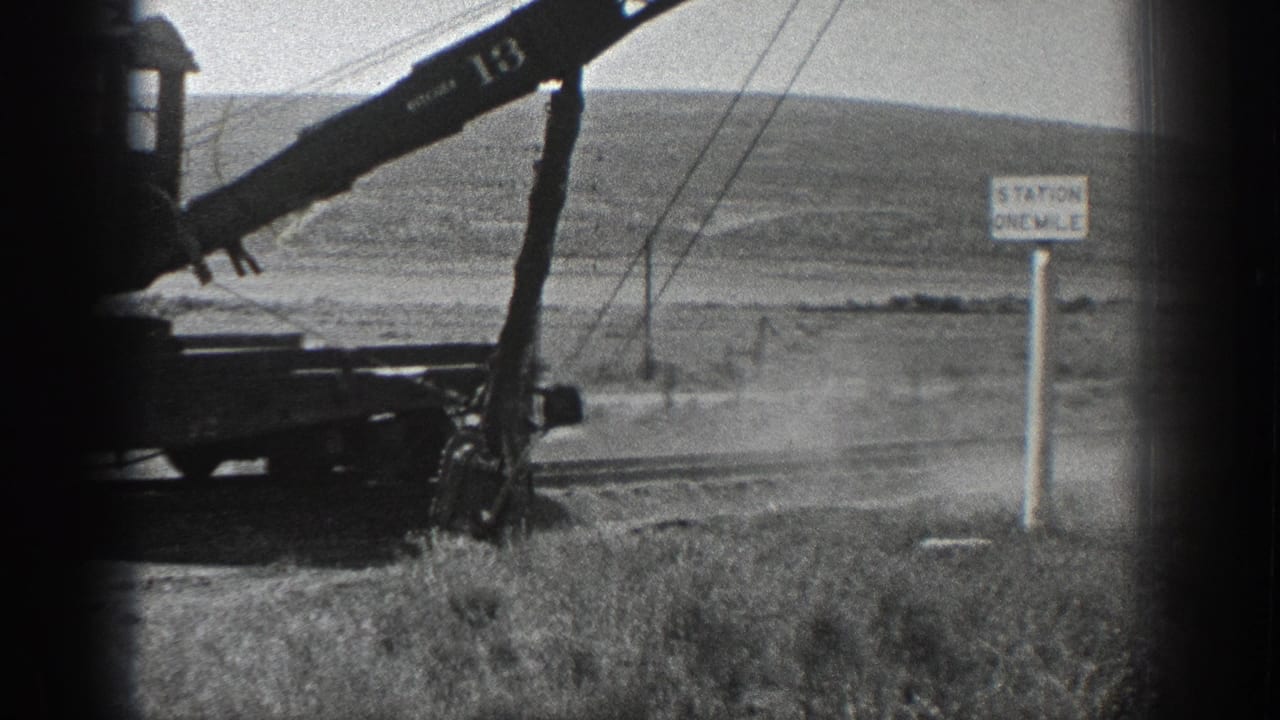 Black-and-white 1936 California frame of a crane marked 13 working near rail infrastructure, with dust, poles, hills, and a station-distance sign.