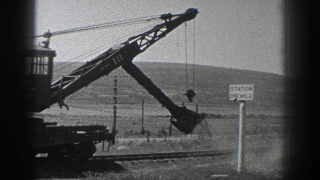 1936 California home-movie frame showing a rail-mounted crane marked 13 with a bucket near a station sign and low hills.