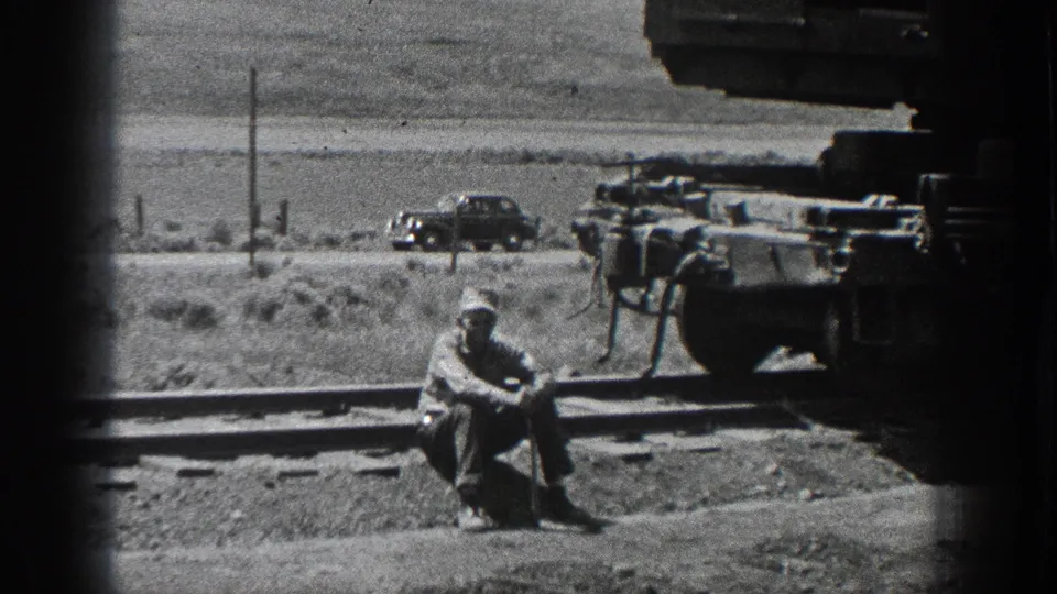 1936 California rail work scene with a crouching worker near tracks, crane machinery at right, and a period car beyond.