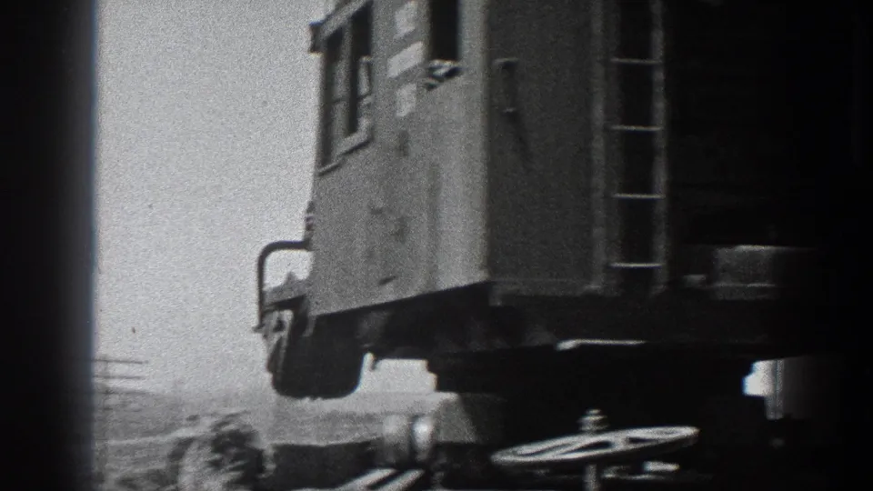 Close home-movie frame of the railcar side and undercarriage, with ladder and wheel hardware visible in harsh outdoor light.
