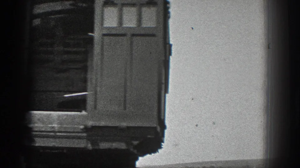 Rear view of the wooden railcar, showing paneled doors, shadowed interior framing, and metal steps beneath the car.