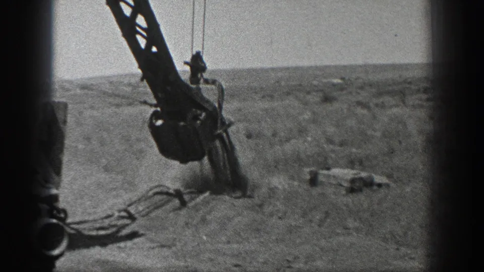 Wide 1936 California frame of the ditcher crane boom and hanging attachment working over open ground.