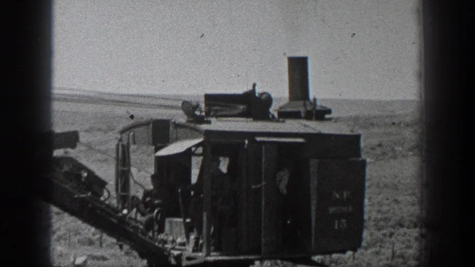 A closer black-and-white frame shows the boxy steam machine cab, roof equipment, and arid California landscape beyond.