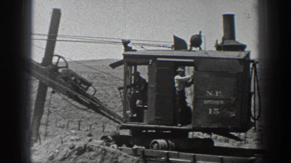 1936 California frame showing the steam excavator, workers, rails, boom, smoke stack, and visible machine markings in a barren work area.