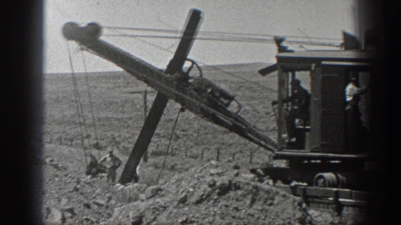 1936 California 8mm frame showing workers near a long-boom excavator on rough railroad construction ground.