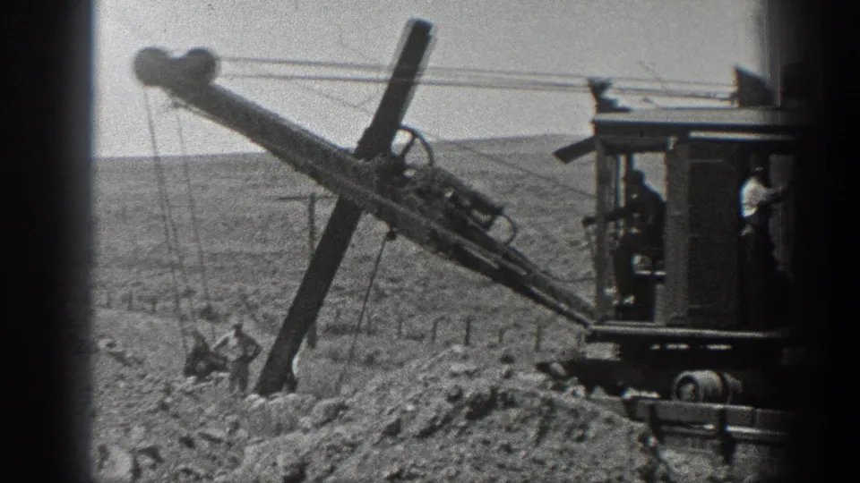 1936 California 8mm frame showing workers near a long-boom excavator on rough railroad construction ground.