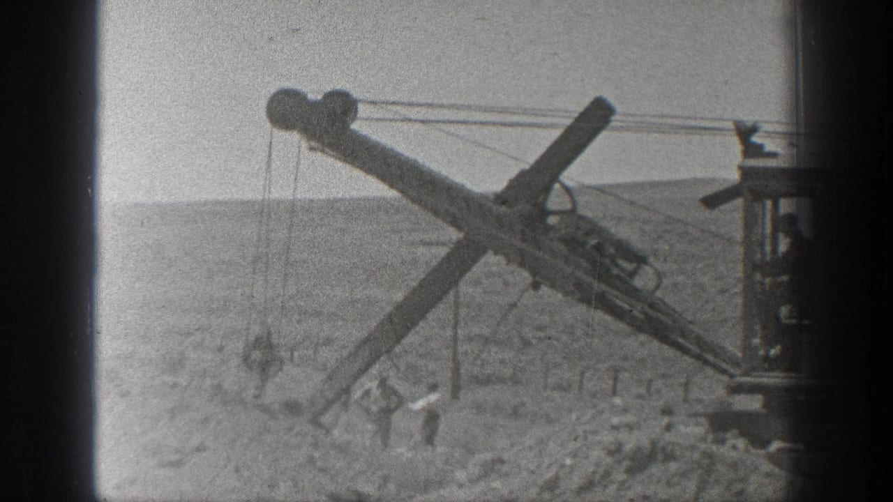Dusty 1936 California frame with a cable excavator arm angled over workers at a railroad construction site.