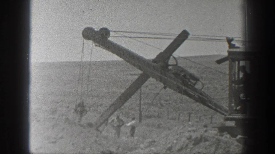 Dusty 1936 California frame with a cable excavator arm angled over workers at a railroad construction site.
