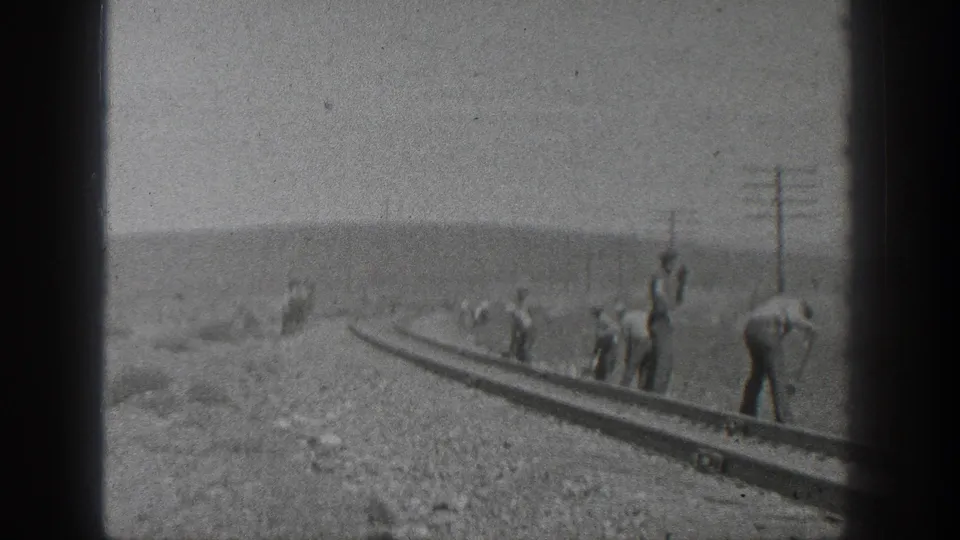 1936 California 8mm view of railroad workers spaced along a rail section, with utility poles and hills beyond.