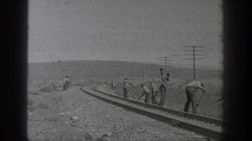 Final 1936 California frame showing workers clustered beside a rail section on a rough construction grade.