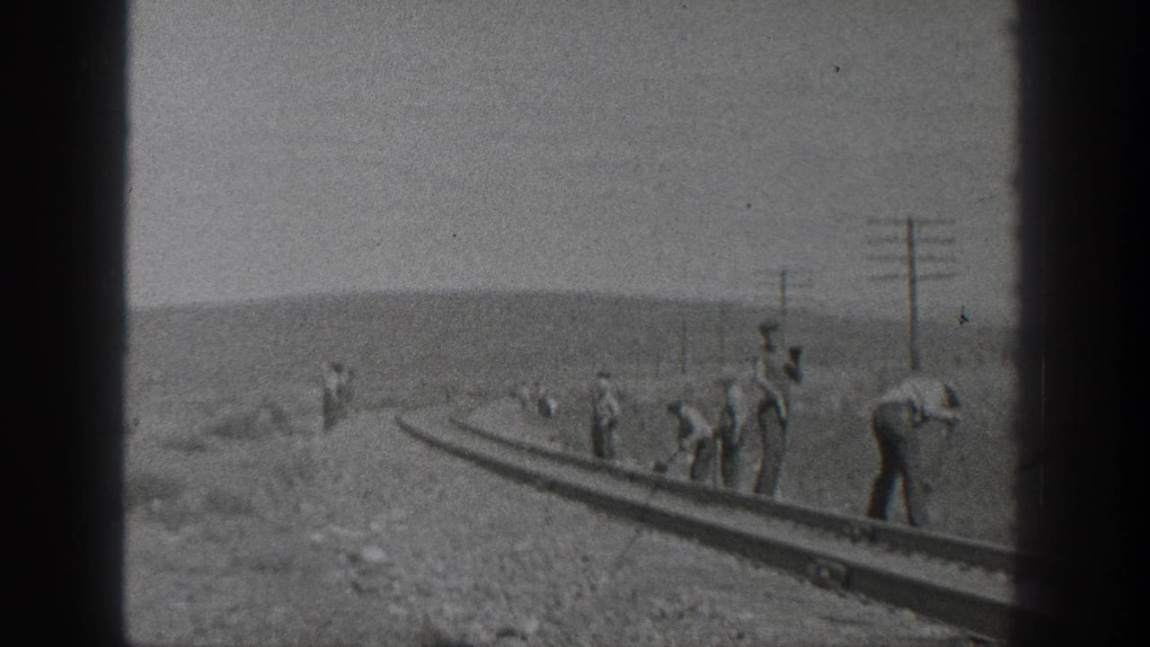 1936 California home-movie frame showing workmen spaced along railway tracks in an arid rural landscape with utility poles behind them.
