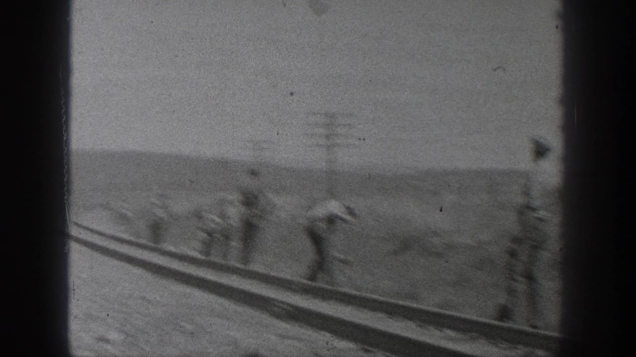Blurred view of men working near railway tracks with utility poles in the distance.