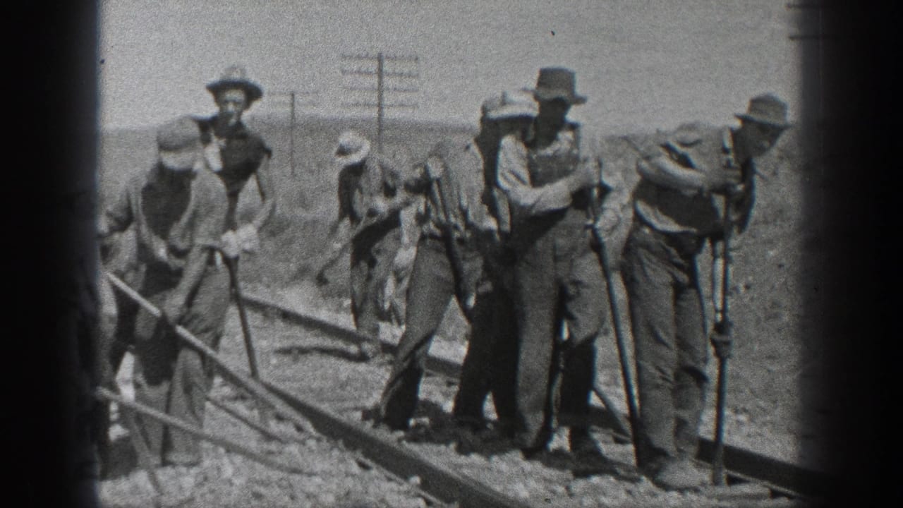 Men in hats stand and work beside railroad tracks in an open desert landscape.