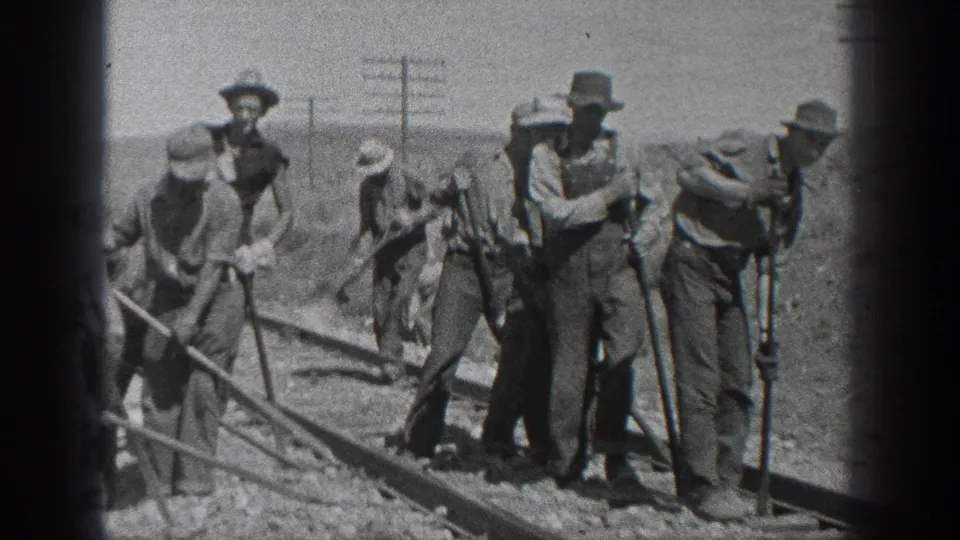 In stated 1936 California footage, several men in work clothes and hats gather along railroad tracks in a desert setting, with tools and utility poles visible behind them.