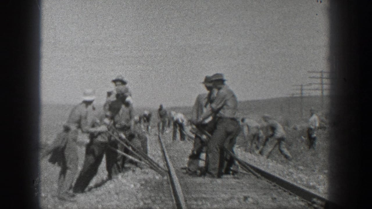 Workers stand and bend near a curved rail line with utility poles in the background.