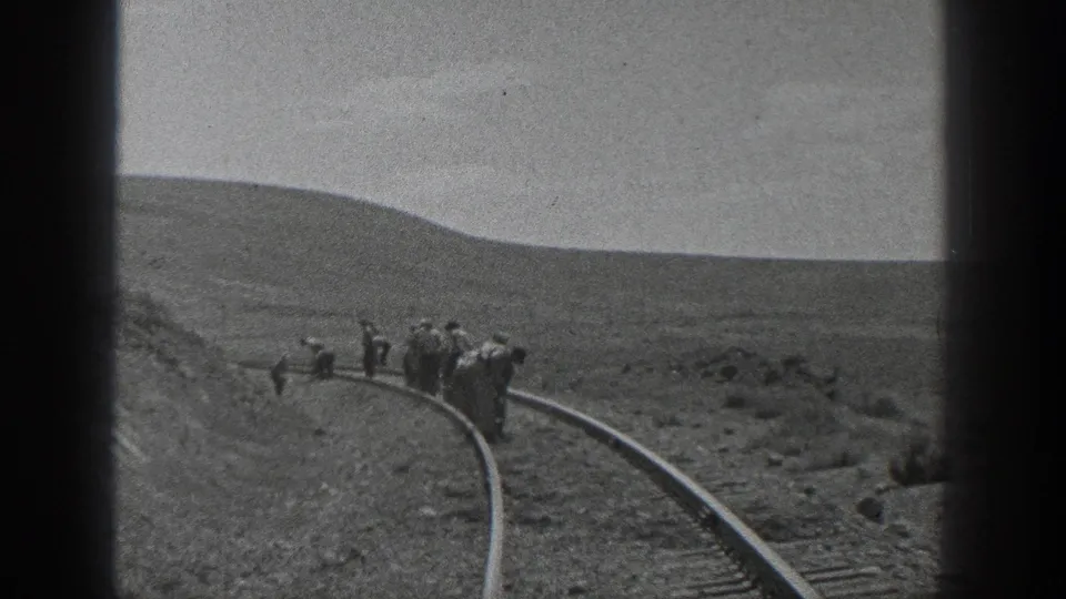 1936 California home-movie frame showing men in hats walking beside a curved railroad track in a dry open landscape.