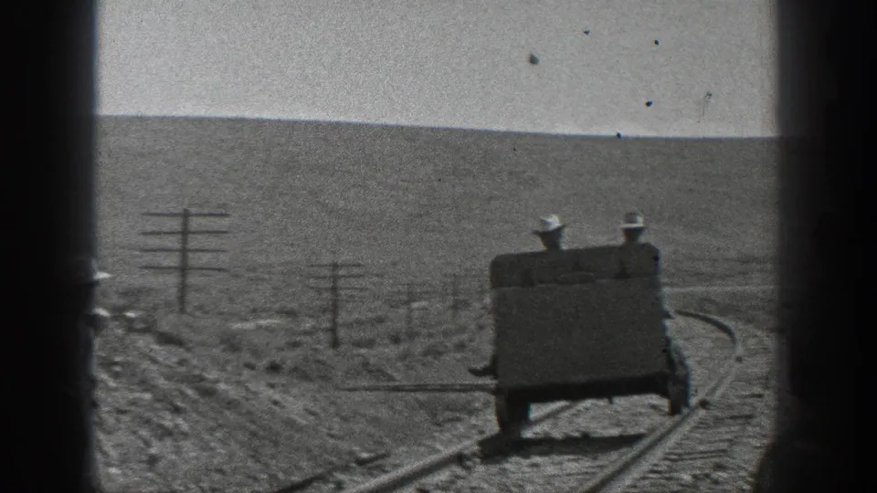 Two men in hats ride a small handcar on a curved railroad track, with utility poles and hills visible in 1936 California footage.