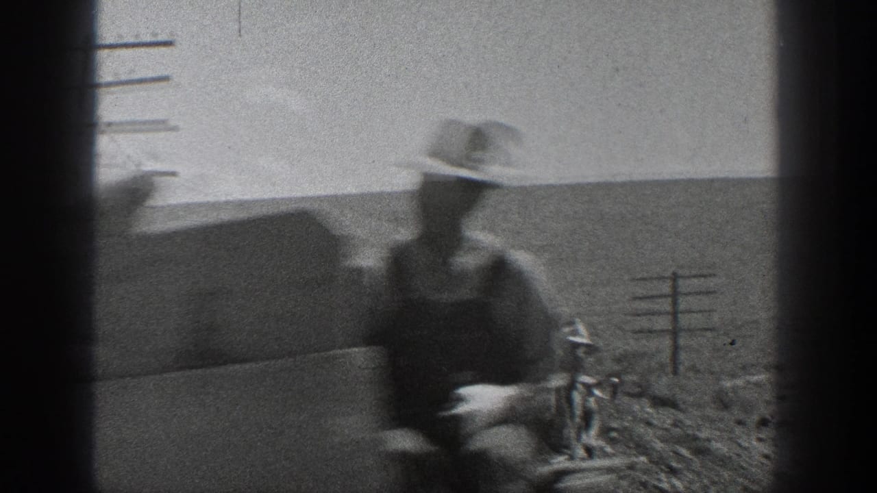 A blurred worker in a brimmed hat stands near railroad tracks in 1936 California, with utility poles and open arid fields behind him.