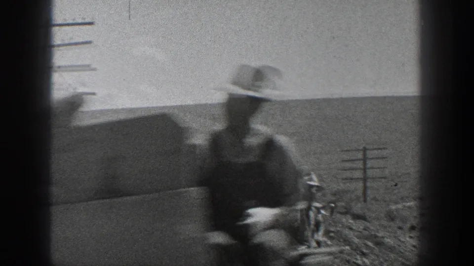 A blurred worker in a brimmed hat stands near railroad tracks in 1936 California, with utility poles and open arid fields behind him.
