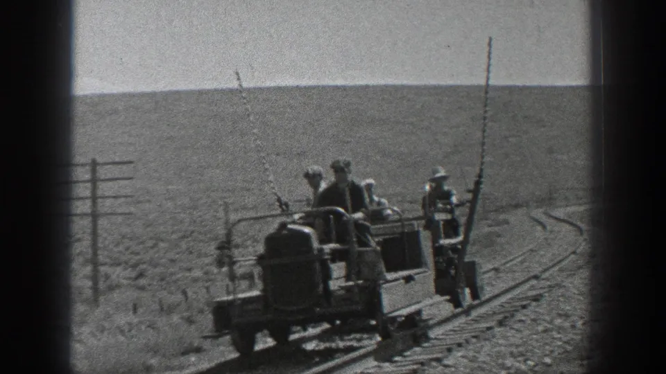 Railroad workers appear on and beside a small maintenance vehicle on curved track in a wide California field.