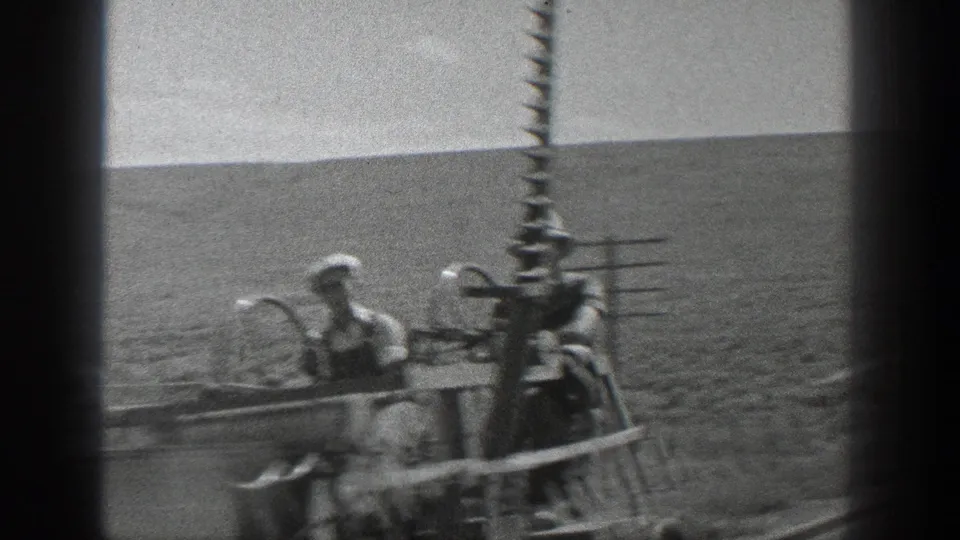 Men in work clothes sit and stand on a small rail vehicle, with poles and a broad open California landscape in view.