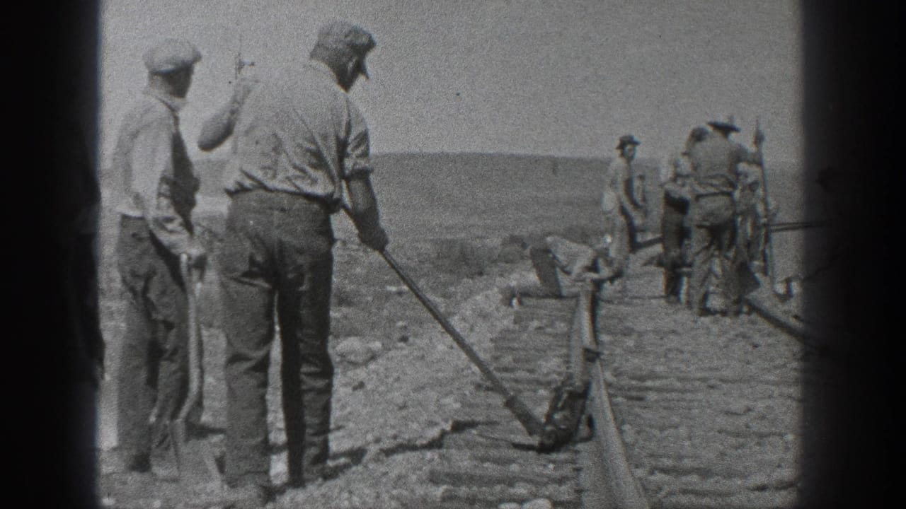 Men work with shovels and tools along railroad tracks in an open landscape.