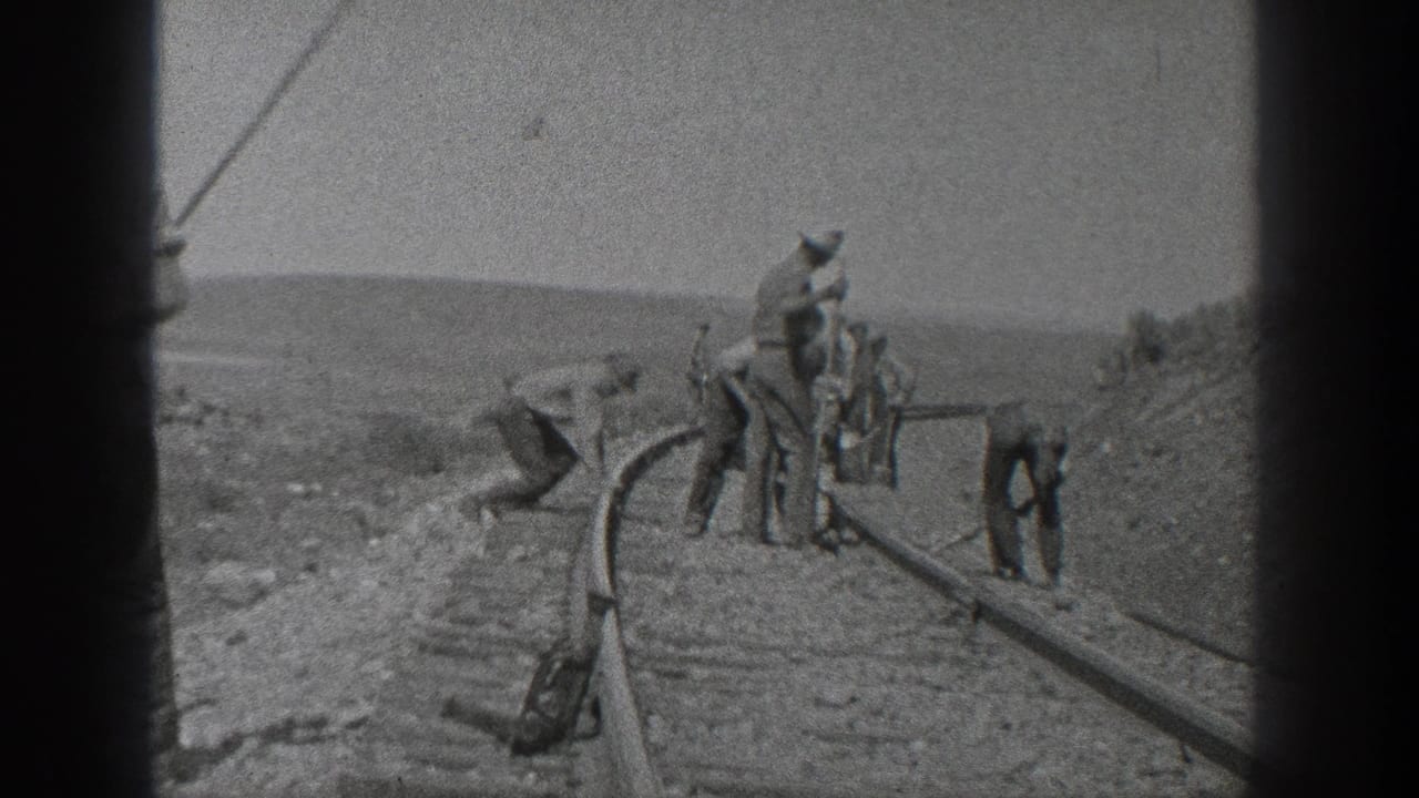 A railroad work crew stands and bends near the tracks with tools.