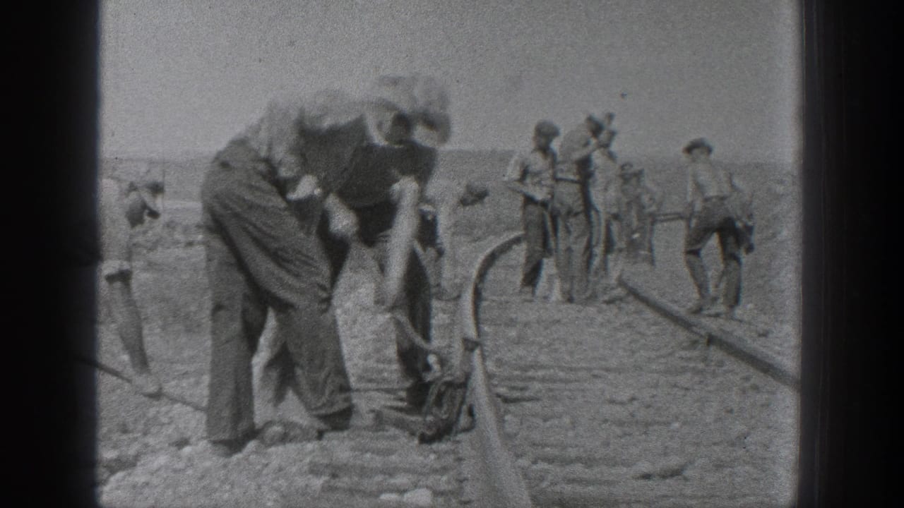 California 1936 home-movie frame showing laborers with hand tools working along railroad tracks in an arid rural setting.