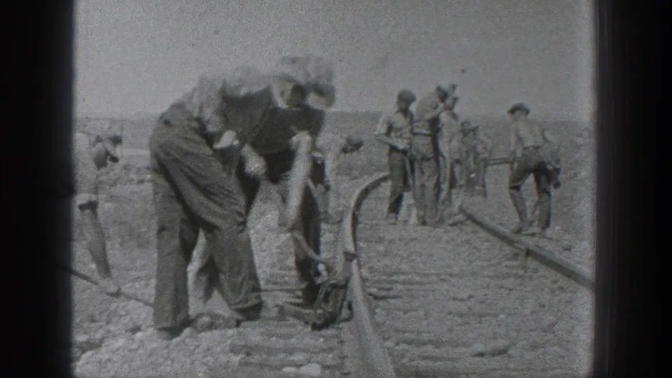 California 1936 home-movie frame showing laborers with hand tools working along railroad tracks in an arid rural setting.