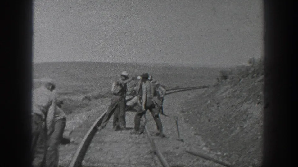 California 1936 frame with several men standing and working beside rail lines near a sloped dirt embankment.