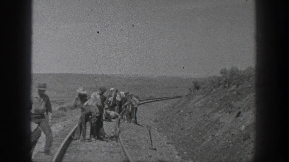 California 1936 frame showing a small railway crew near curved rail lines, hand tools, and a sloped arid embankment.