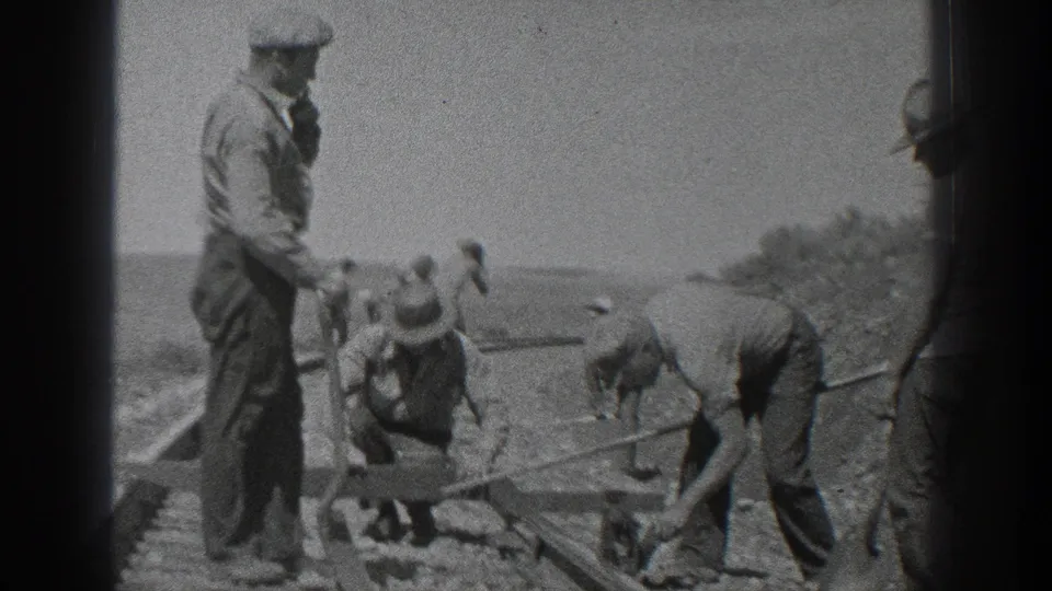 Several workers adjust railroad ties and rails while others stand close by in the supplied 1936 California rural work scene.