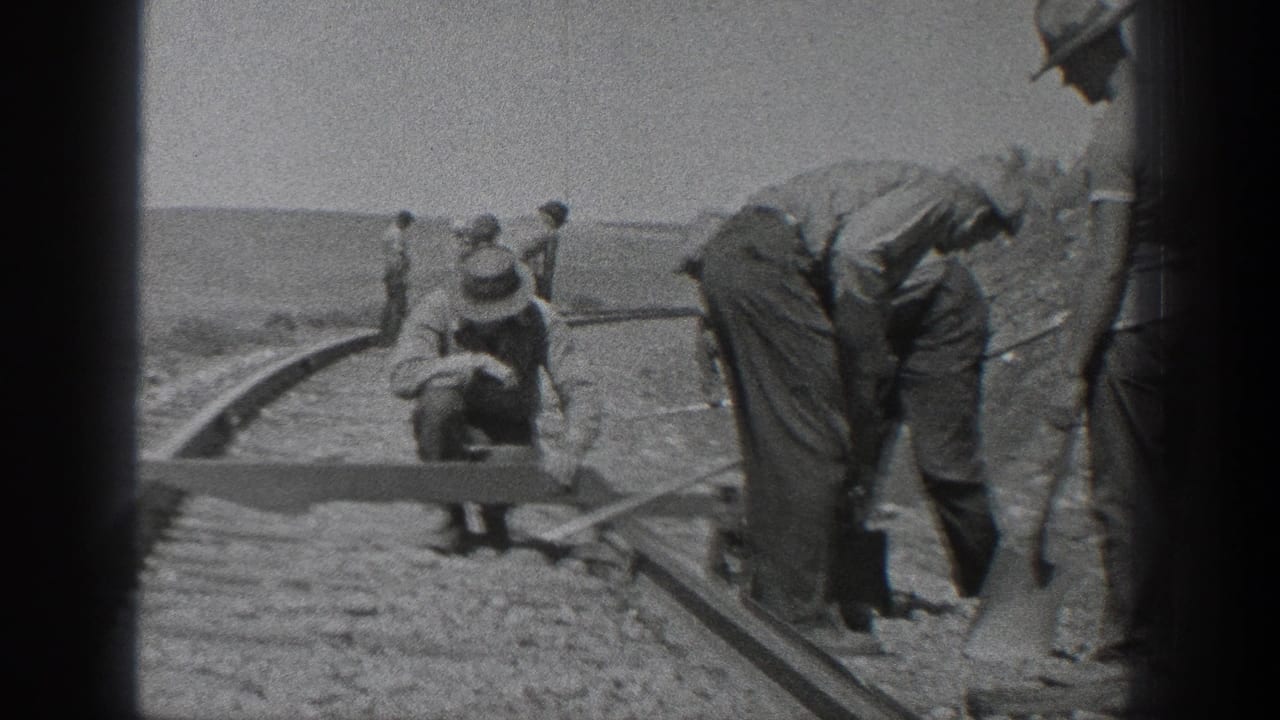California 1936 home-movie frame showing men in hats and work clothes gathered along a curved rail line under open sky.