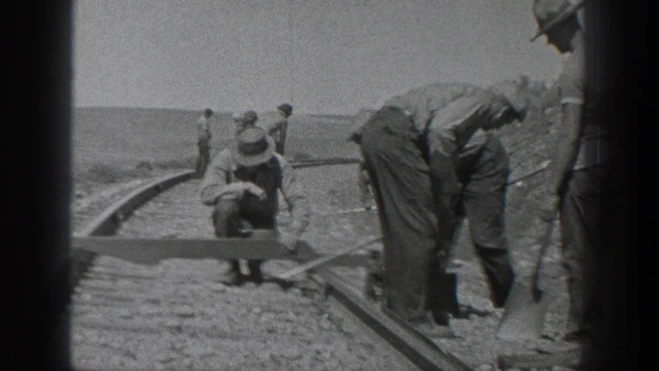 California 1936 home-movie frame showing men in hats and work clothes gathered along a curved rail line under open sky.