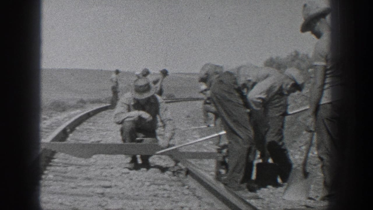 Men work close to the rail, with one crouching and others bending near the track.