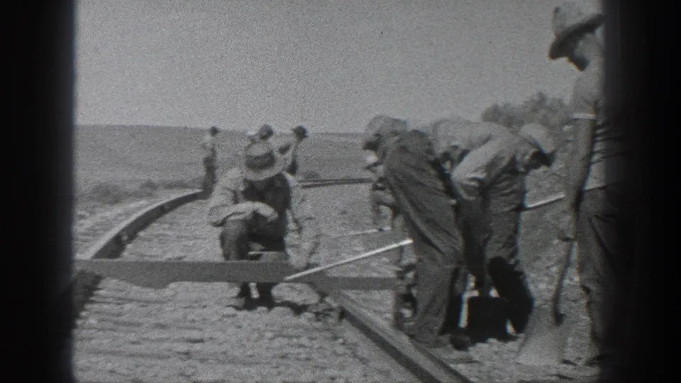 California 1936 frame of railroad laborers bending and crouching beside a curved track in an arid outdoor setting.