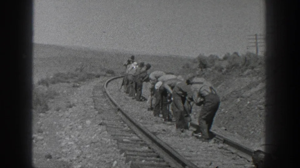 California 1936 frame showing a crew spread along a curved railroad track, many bending to work near the rail bed.