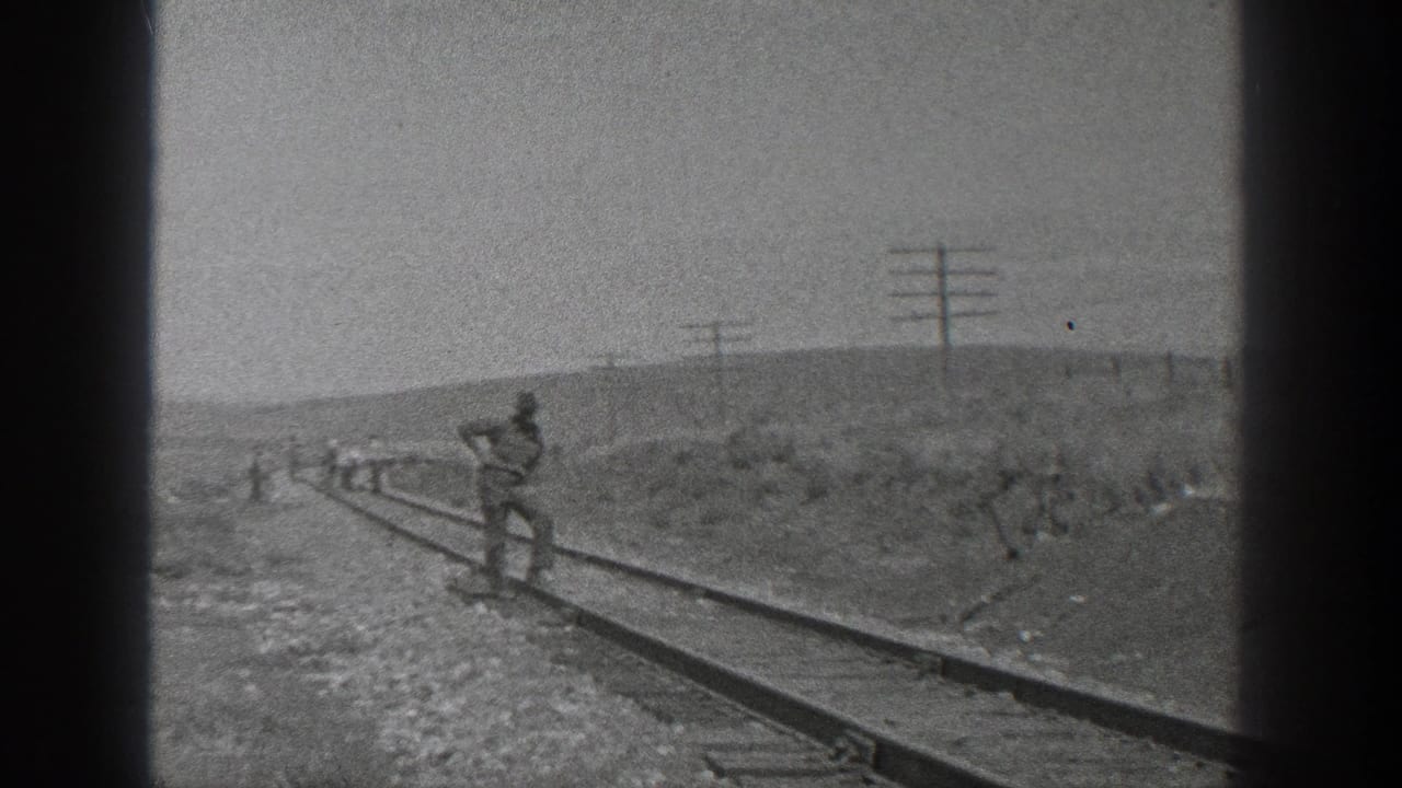 A man stands on railroad tracks while a work crew is visible in the distance.