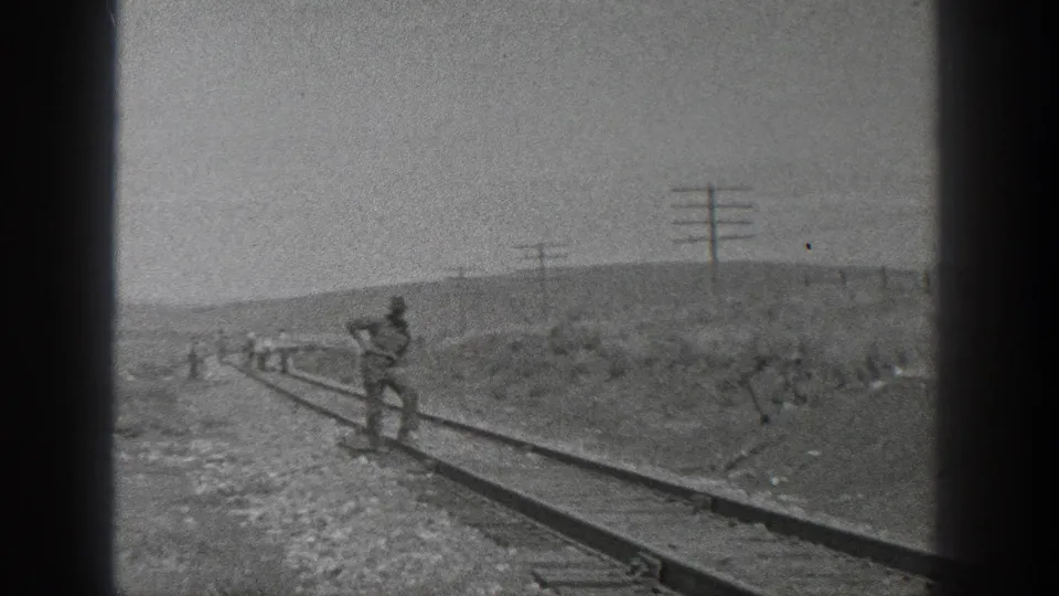 A worker stands near the rails in rural California, with other men spread along the track in the distance.