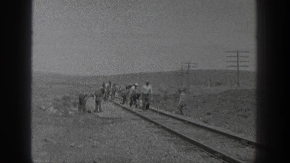A group of adult workers clusters along the rail line in the stated 1936 California setting, with utility poles and low hills behind them.
