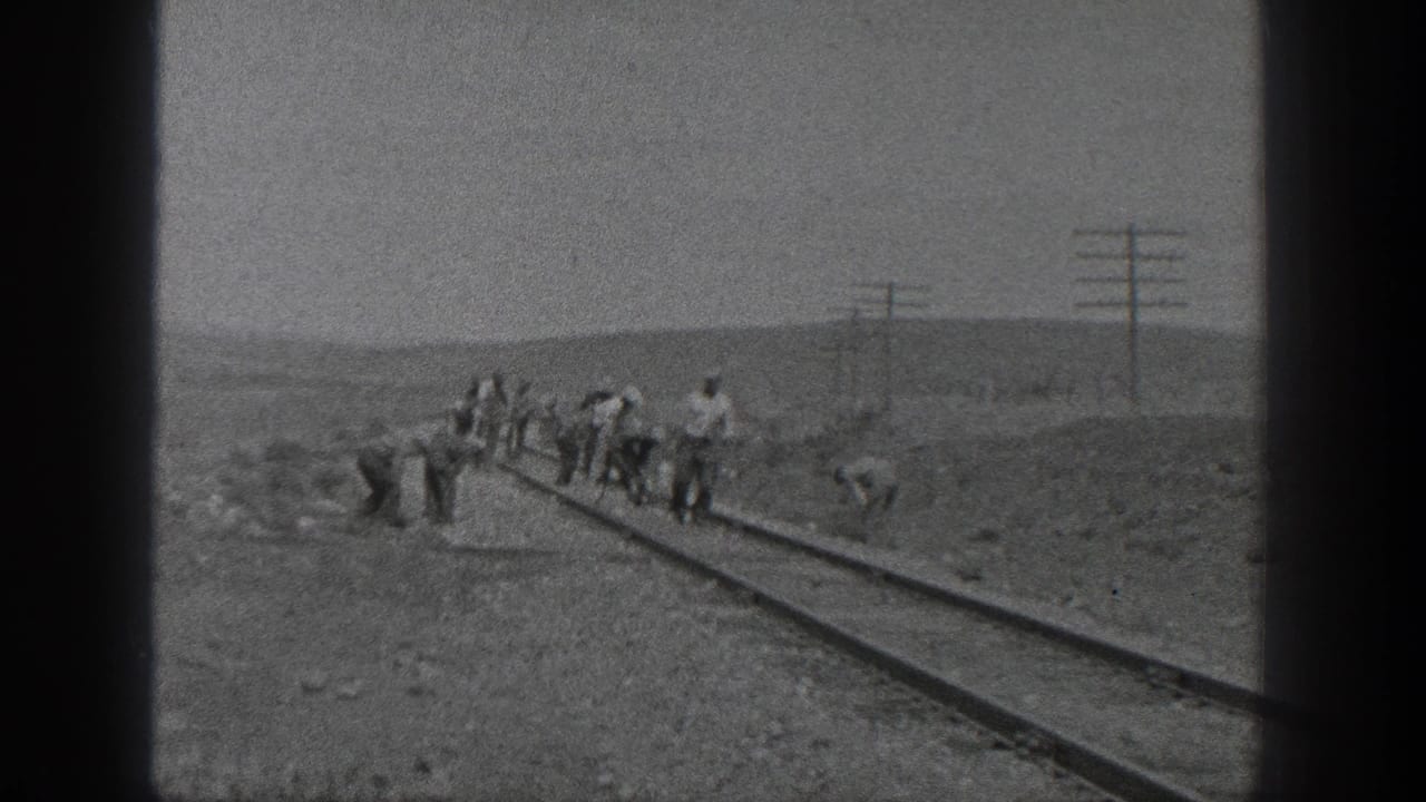 1936 California 8mm frame showing a crew working along railroad tracks with utility poles and low hills in the distance.