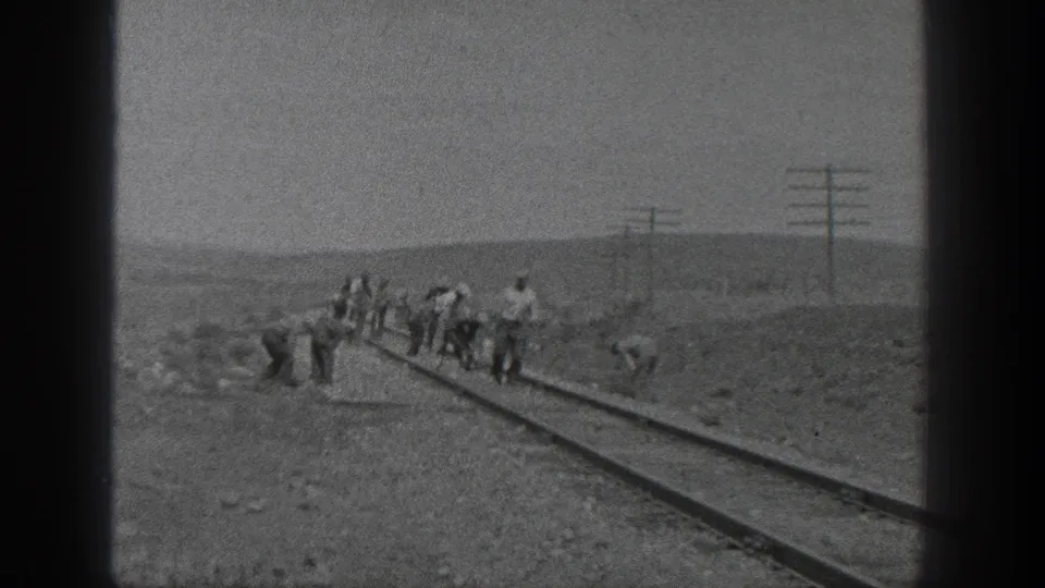 1936 California 8mm frame showing a crew working along railroad tracks with utility poles and low hills in the distance.
