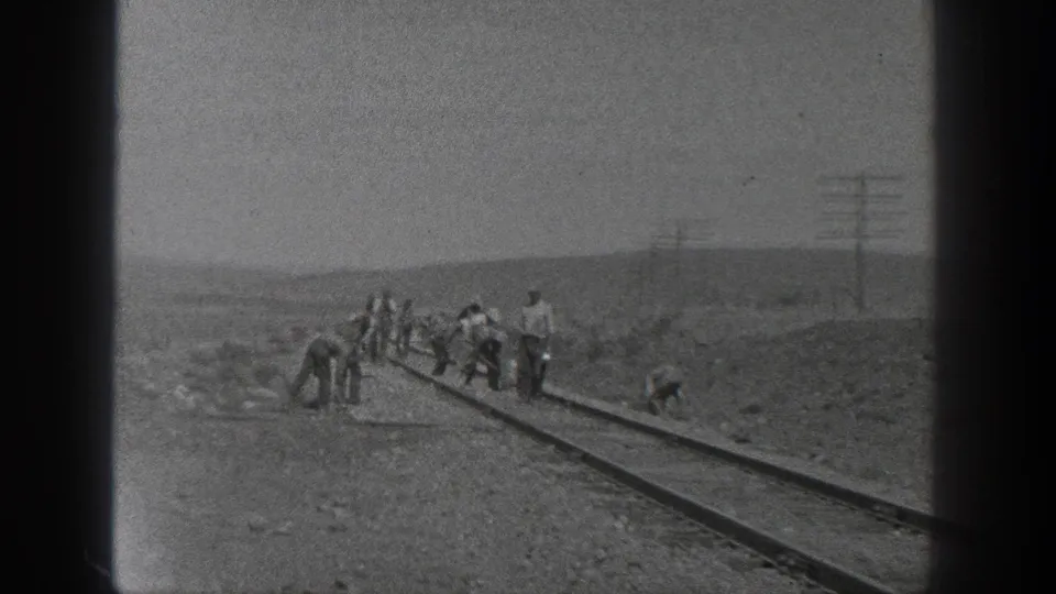 A rural California railroad crew appears to work by hand on the rails, with poles and low hills behind them.